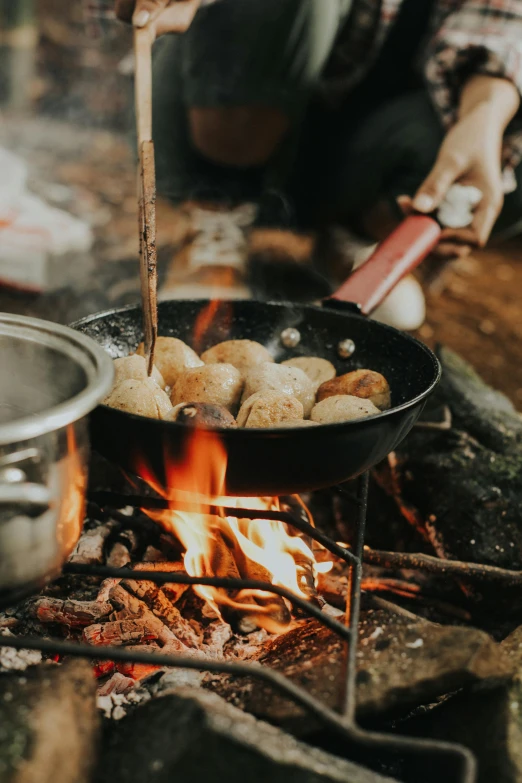 a person cooking food over an open fire, puffballs, adventure gear, black