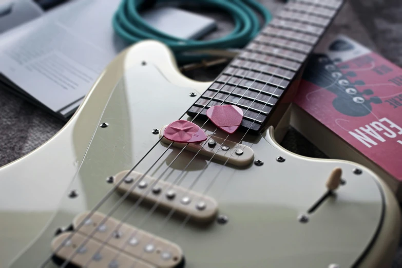 a guitar sitting on top of a table next to a book, heart effects, fender stratocaster, petals, zoomed in