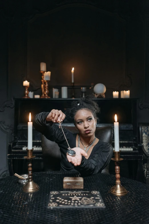 a woman sitting at a table with candles in front of her, pexels contest winner, vanitas, holding a wand, promotional photo, black rococo, alexis franklin