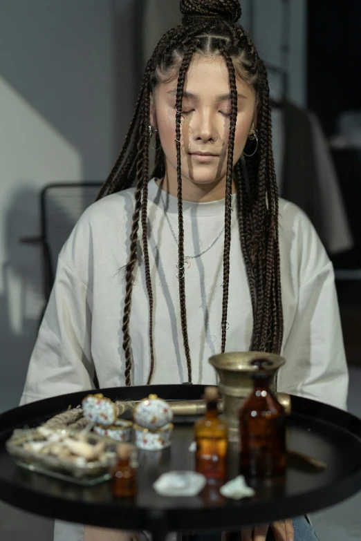 a woman holding a tray with food on it, inspired by Kim Tschang Yeul, trending on pexels, hyperrealism, box braids, apothecary, put on a mannequin, sitting at a table