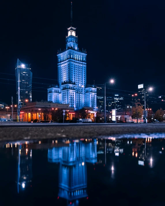 a clock tower in the middle of a city at night, a colorized photo, by Julia Pishtar, unsplash contest winner, socialist realism, the building is a skyscraper, warsaw, lgbtq, photo of putin