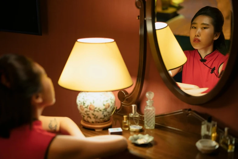 a woman sitting at a desk in front of a mirror, inspired by Nan Goldin, pexels contest winner, wearing a red cheongsam, avatar image, hotel room, ( ( theatrical ) )