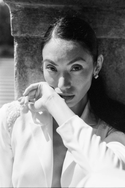 a black and white photo of a woman leaning against a wall, inspired by Li Di, wearing white suit, ashteroth, hand on her chin, lucy liu portrait