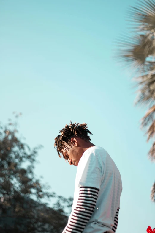 a man riding a skateboard down the side of a road, an album cover, trending on pexels, palm tree, xxxtentacion, side profile waist up portrait, wearing a white sweater
