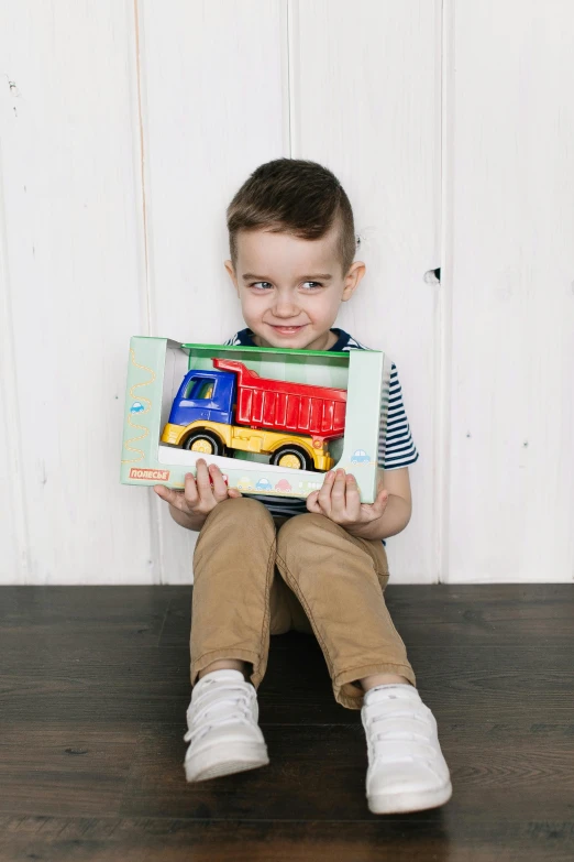 a little boy sitting on the floor holding a box of books, inspired by Sam Havadtoy, trucks, multicoloured, textured, blippi