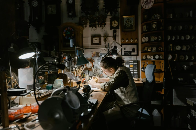 a woman sitting at a table working on a piece of art, by Matthias Stom, pexels contest winner, arts and crafts movement, a steampunk store, in his basement studio, avatar image, kris kuksi