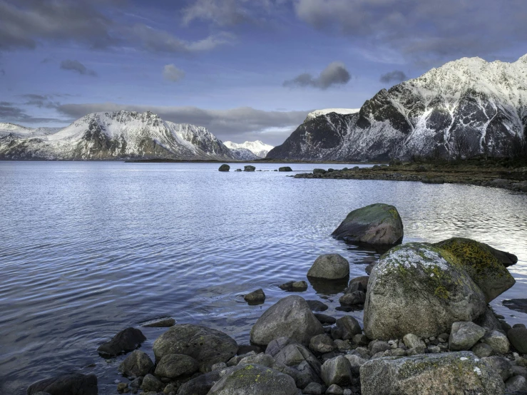 a large body of water with mountains in the background, by Roar Kjernstad, pexels contest winner, boulders, snowy fjord, elegant