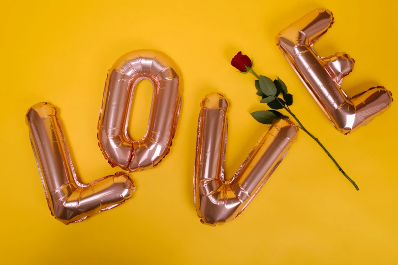 balloons spelling love and a rose on a yellow background, by Julia Pishtar, trending on pexels, romanticism, foil, rose gold, museum quality photo, 🐿🍸🍋