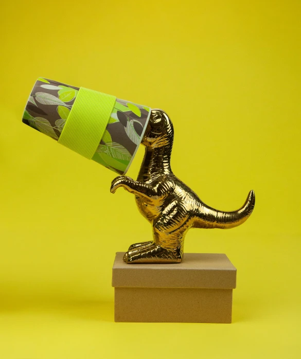 a toy t - rex with a green tube sticking out of it's mouth, a surrealist sculpture, inspired by Sarah Lucas, magic realism, gold dappled lighting, chocolate, epic award winning, cardboard