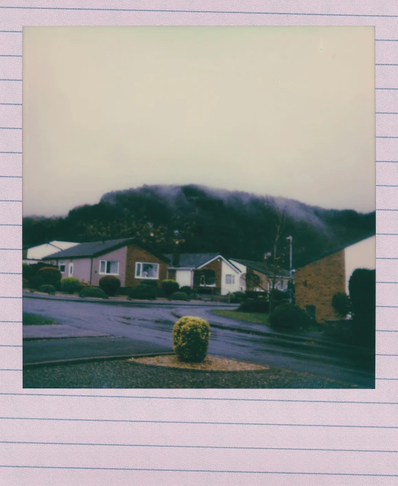 a picture of a house with a mountain in the background, a polaroid photo, hazy and misty, suburbia street, black mountains, pastel overflow