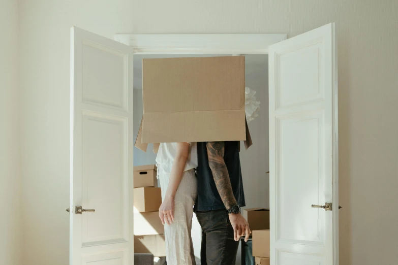 a man standing in a doorway with a cardboard box on his head, pexels contest winner, man and woman in love, house interior, covered chest, top of pinterest