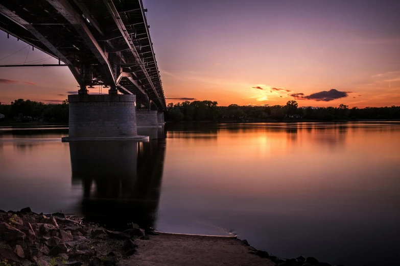 a bridge over a body of water at sunset, by Antoni Brodowski, pexels contest winner, red river, 85mm nd 5, under bridge, purple glow