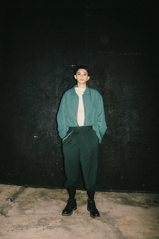 a woman standing in front of a black wall, an album cover, unsplash, sea - green and white clothes, androgyny, tomohiro shimoguchi, wearing a track suit