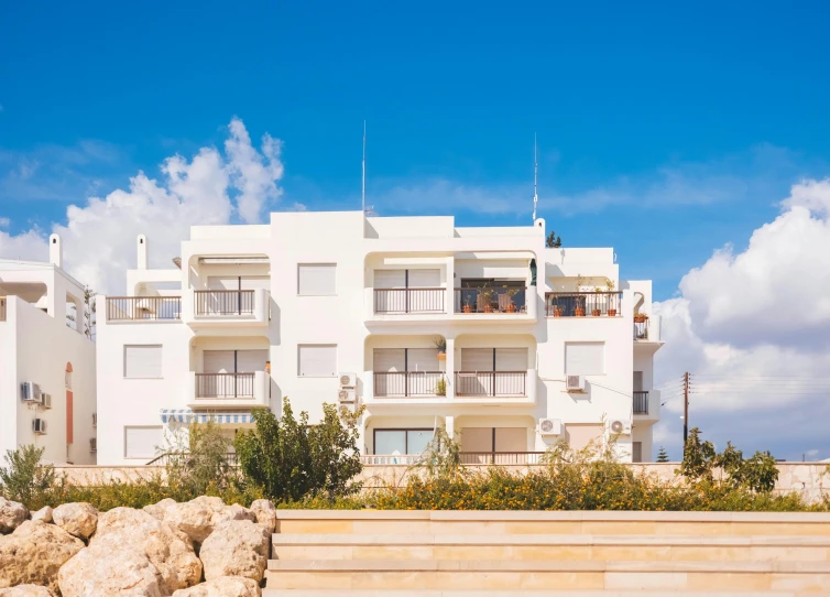 a large white building next to a body of water, unsplash, bauhaus, cyprus, apartments, white travertine terraces, blue skies