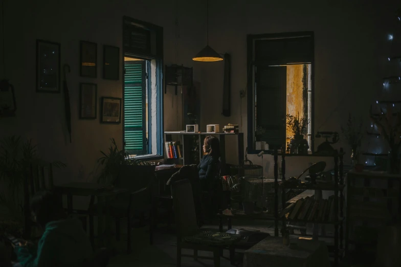 a person sitting at a table in a dark room, a picture, inspired by Elsa Bleda, unsplash contest winner, australian tonalism, inside an old apartment, dusty library, cinematic. by leng jun, the golden hour