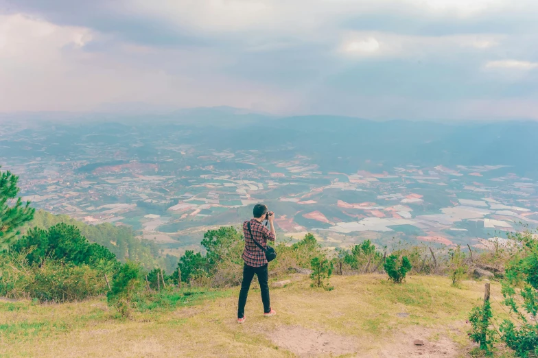 a man standing on top of a lush green hillside, pexels contest winner, sumatraism, panoramic view of girl, coloured film photography, overlooking, shan shui