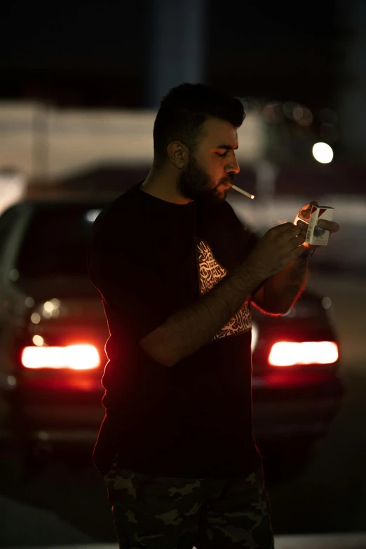 a man smoking a cigarette on a street at night, by Ahmed Yacoubi, standing in a parking lot, booze, smoking a cigarrette🚬, arab