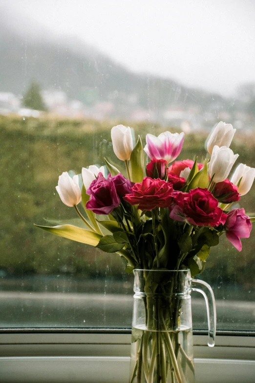 a vase of flowers sitting on a window sill, trending on unsplash, romanticism, rain storm, roses and tulips, lake view, like a catalog photograph