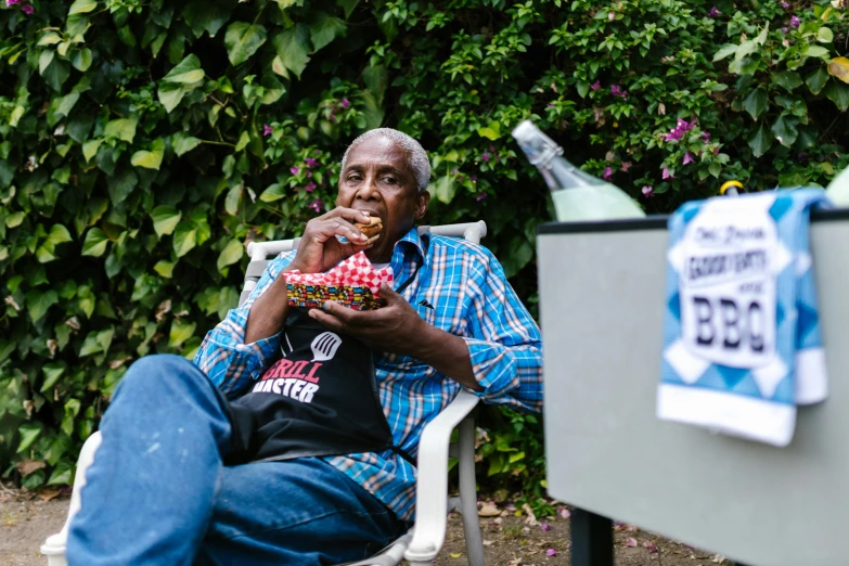 a man sitting in a chair eating a donut, a portrait, by Joe Bowler, pexels contest winner, barbecue, grandfatherly, people on a picnic, black man