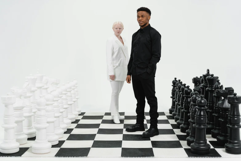 a man and a woman standing next to a giant chess board, an album cover, pexels contest winner, bowater charlie and brom gerald, black main color, in front of white back drop, non-binary