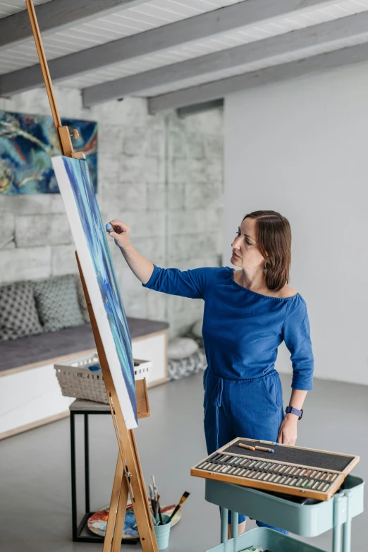 a woman standing in front of a painting on a easel, inspired by Jan Kupecký, pexels contest winner, architect studio, ocean of canvas catching fire, on a white table, portrait of small