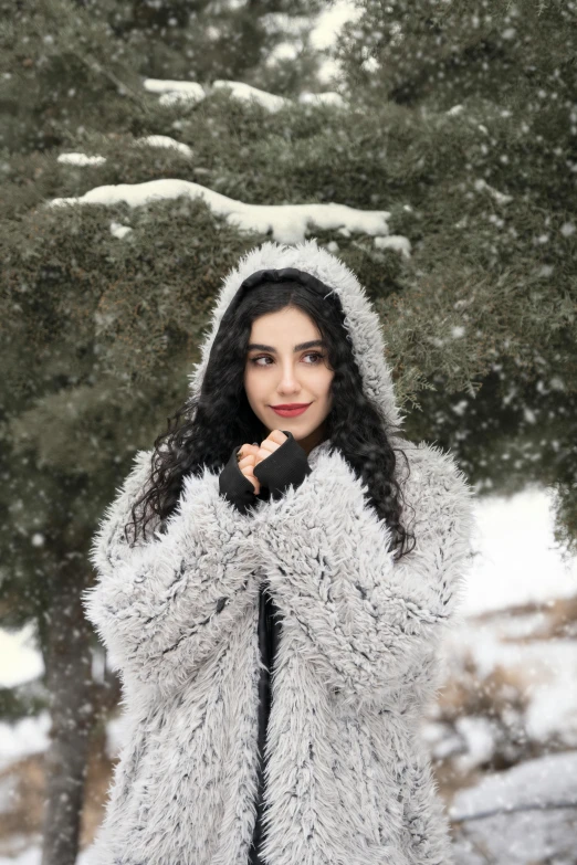 a woman in a furry coat standing in the snow, by Maryam Hashemi, trending on pexels, young middle eastern woman, with curly black and silver hair, wearing festive clothing, girl wearing hoodie