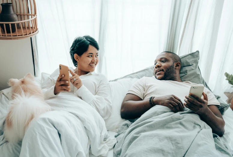 a man and woman laying in bed with a dog, trending on pexels, happening, looking at his phone, wearing white robes, varying ethnicities, good friends