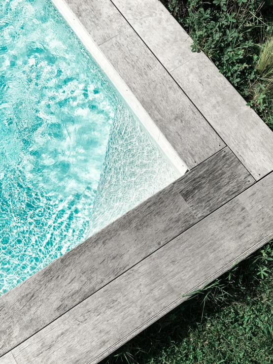 a pool sitting on top of a lush green field, inspired by Tadao Ando, unsplash contest winner, white and teal metallic accents, wood effect, close - up photograph, trending on vsco