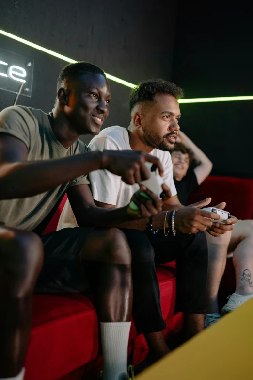 a group of men sitting on top of a red couch, ea sport, adut akech, playing video games, lgbtq