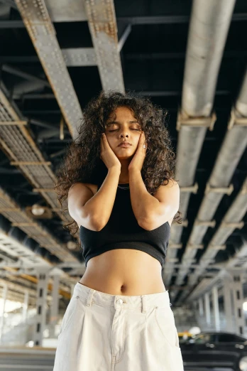 a woman in a black top and white pants, by Niko Henrichon, trending on pexels, renaissance, stressed expression, black curly hair, bridge, physical : tinyest midriff ever