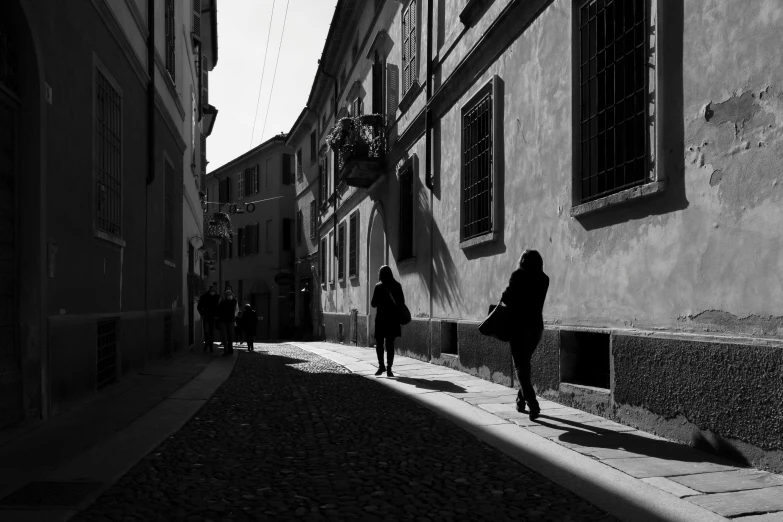 a black and white photo of people walking down a street, by Andrea Orcagna, pexels contest winner, deep shadows and colors, bizzaro, bright sunny day, in the early morning