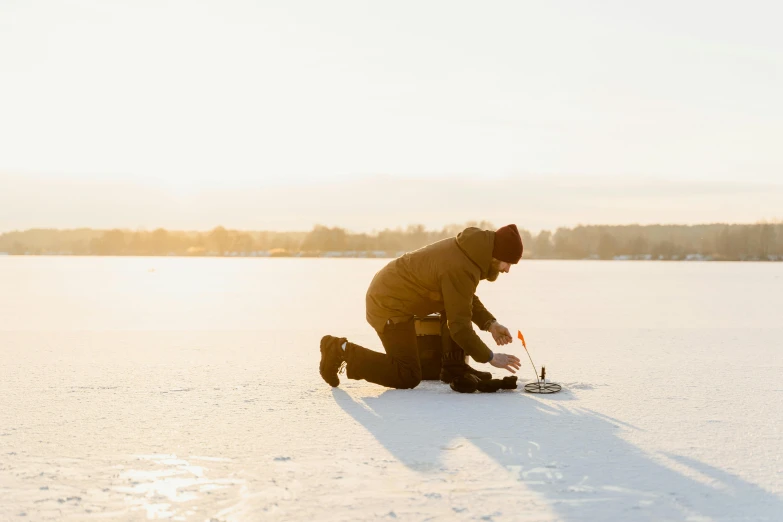 a man kneeling on top of a snow covered field, by Julia Pishtar, pexels contest winner, fishing, ice fish shape, warm light, thumbnail