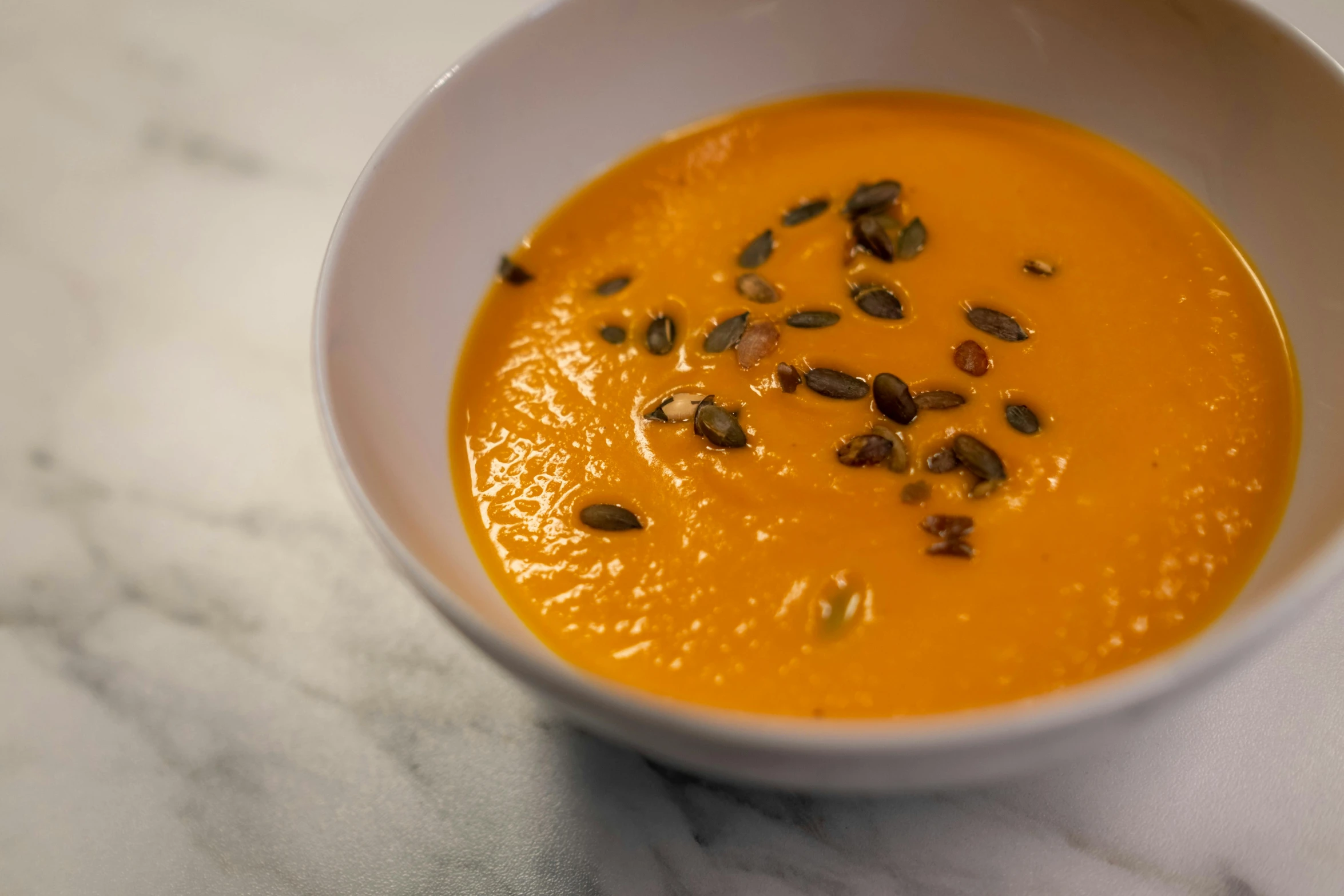 a close up of a bowl of soup on a table, vibrant but dreary orange, seeds, glossy surface, pumpkin