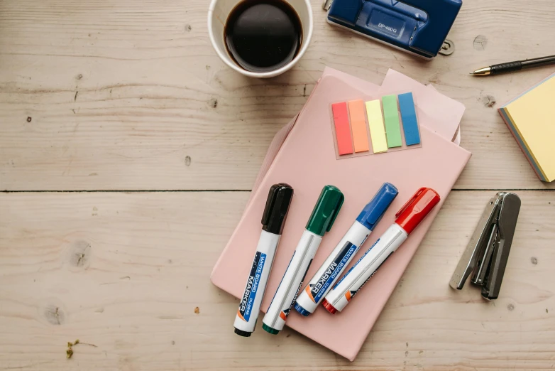 a wooden table topped with office supplies and a cup of coffee, coloured marker, blue and green and red tones, thumbnail, whiteboards