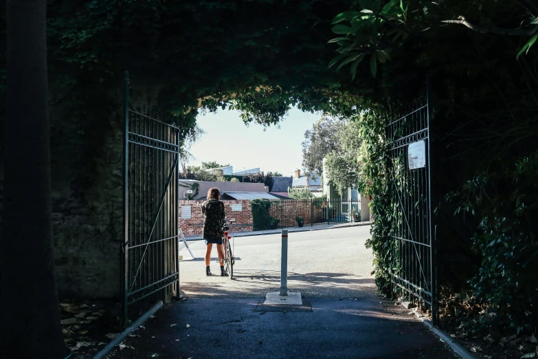 a person standing in front of an open gate, by Nina Hamnett, unsplash, north melbourne street, private school, vine covered, in the middle of a small colony