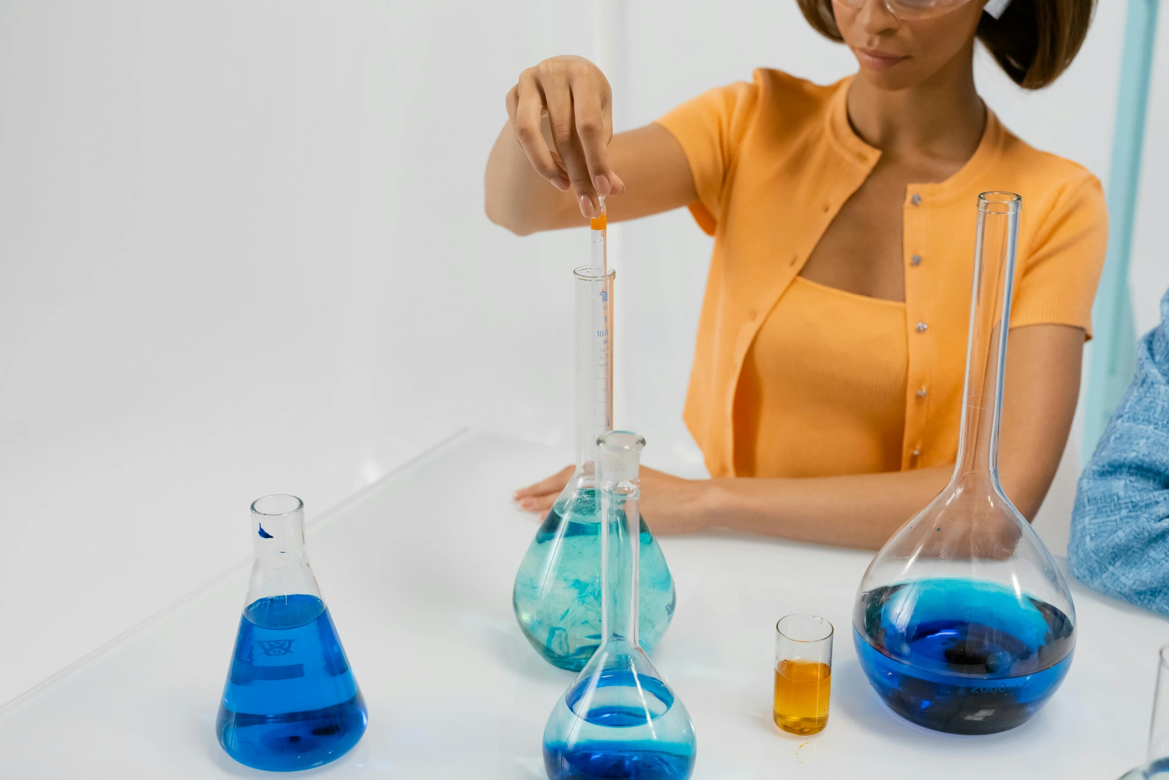 a woman holding a flask filled with blue liquid, trending on pexels, analytical art, balancing the equation, chartreuse and orange and cyan, vials, school class