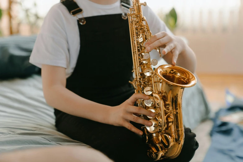 a little boy sitting on a bed playing a saxophone, trending on pexels, female, resin, waist high, ( mechanical )