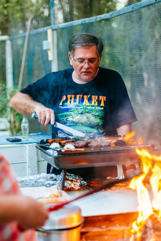 a man is cooking food on a grill, by Elizabeth Durack, dinner is served, fish in the background, mike, community celebration