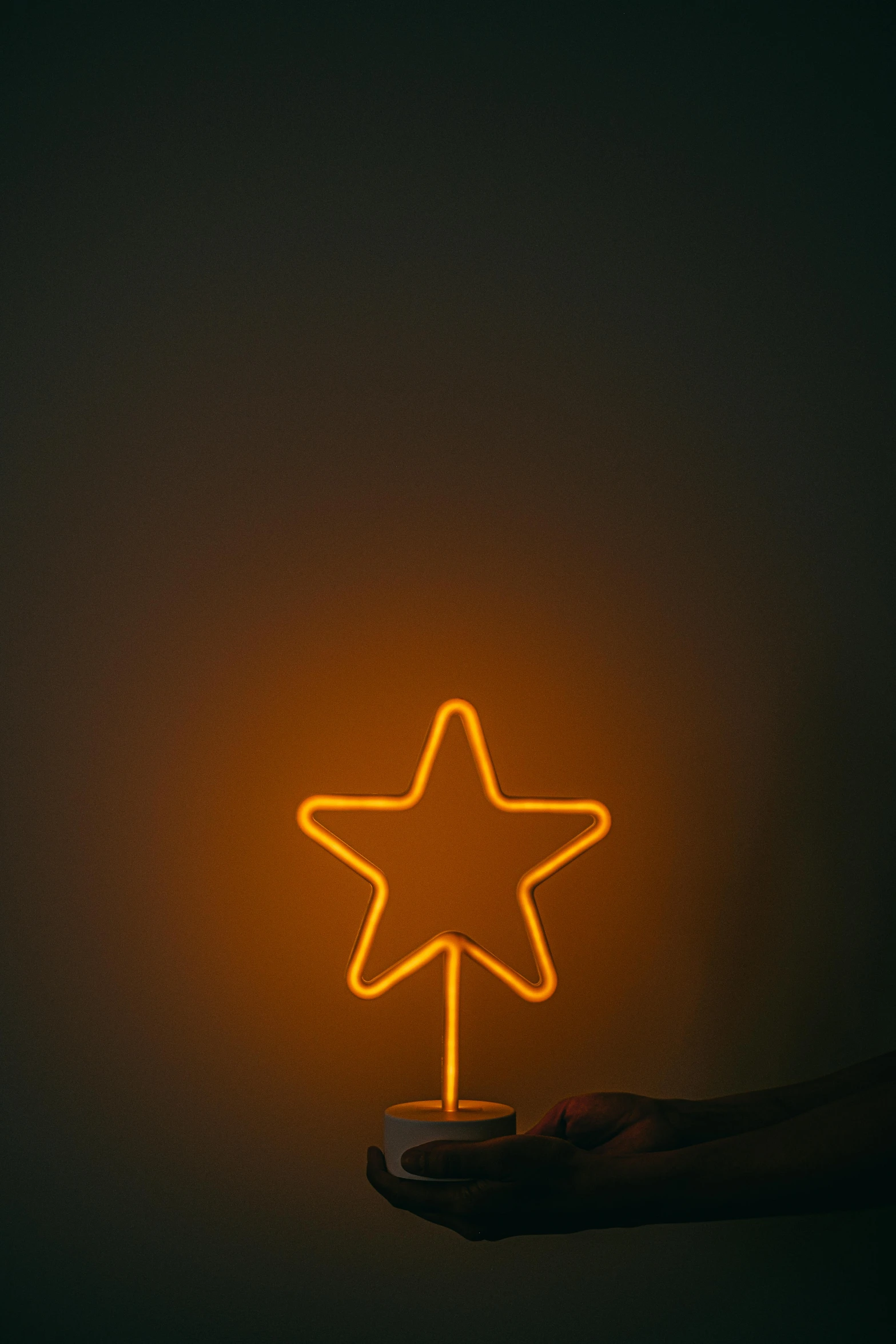 a person holding a neon star in their hand, by Attila Meszlenyi, minimalism, yellow-orange, made of wire, star base, sweet night ambient