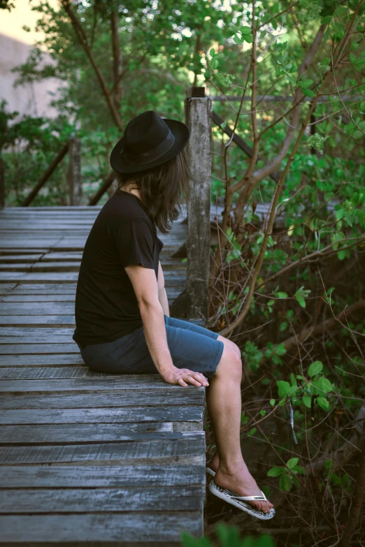 a woman sitting on top of a wooden bridge, pexels contest winner, black hat, androgynous male, aboriginal australian hipster, lush surroundings