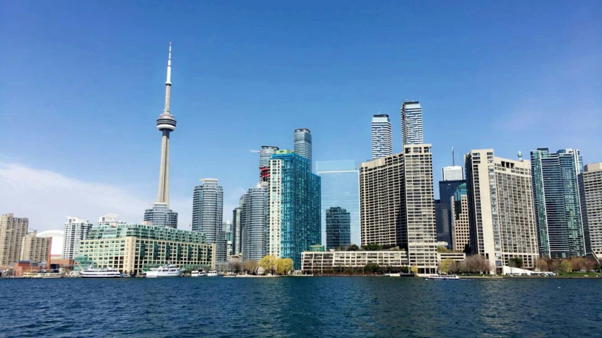 a large body of water with tall buildings in the background, a photo, cn tower, clear blue skies, youtube thumbnail, splash image
