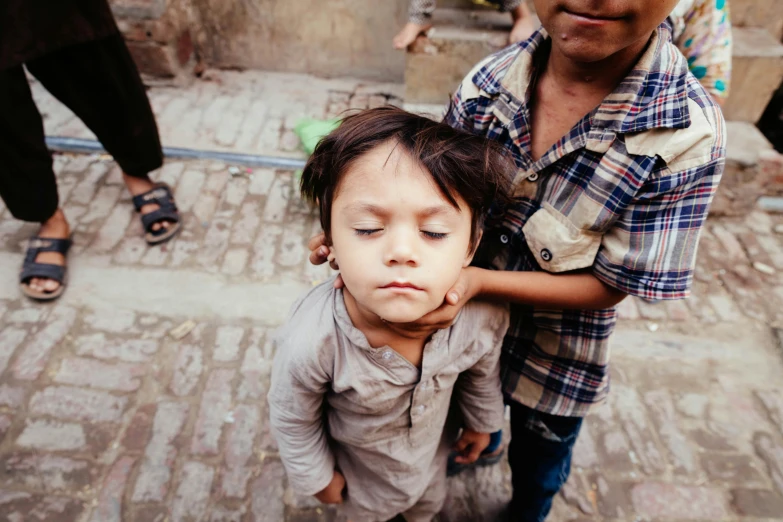 a couple of kids standing next to each other, pexels contest winner, tight around neck, on an indian street, sleepy, young child