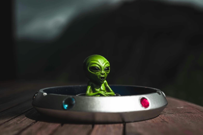 a toy alien sitting in a ring on a wooden table, alien shop, shot with sony alpha 1 camera, ashtray, instagram picture