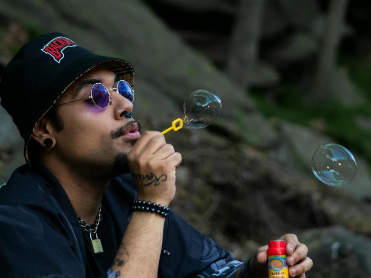 a man blowing bubbles while sitting on a rock, an album cover, pexels contest winner, wearing sunglasses and a cap, raden saleh, 🚀🌈🤩, wiz khalifa