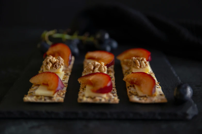 a black plate topped with crackers covered in fruit, inspired by Orazio Gentileschi, unsplash, walnuts, 6 pack, professional product shot, cheesy