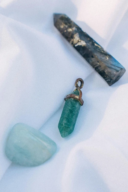 a couple of stones sitting on top of a white sheet, inspired by Elsa Bleda, trending on unsplash, close up shot of an amulet, cyan and green, made of crystal, detailed product image