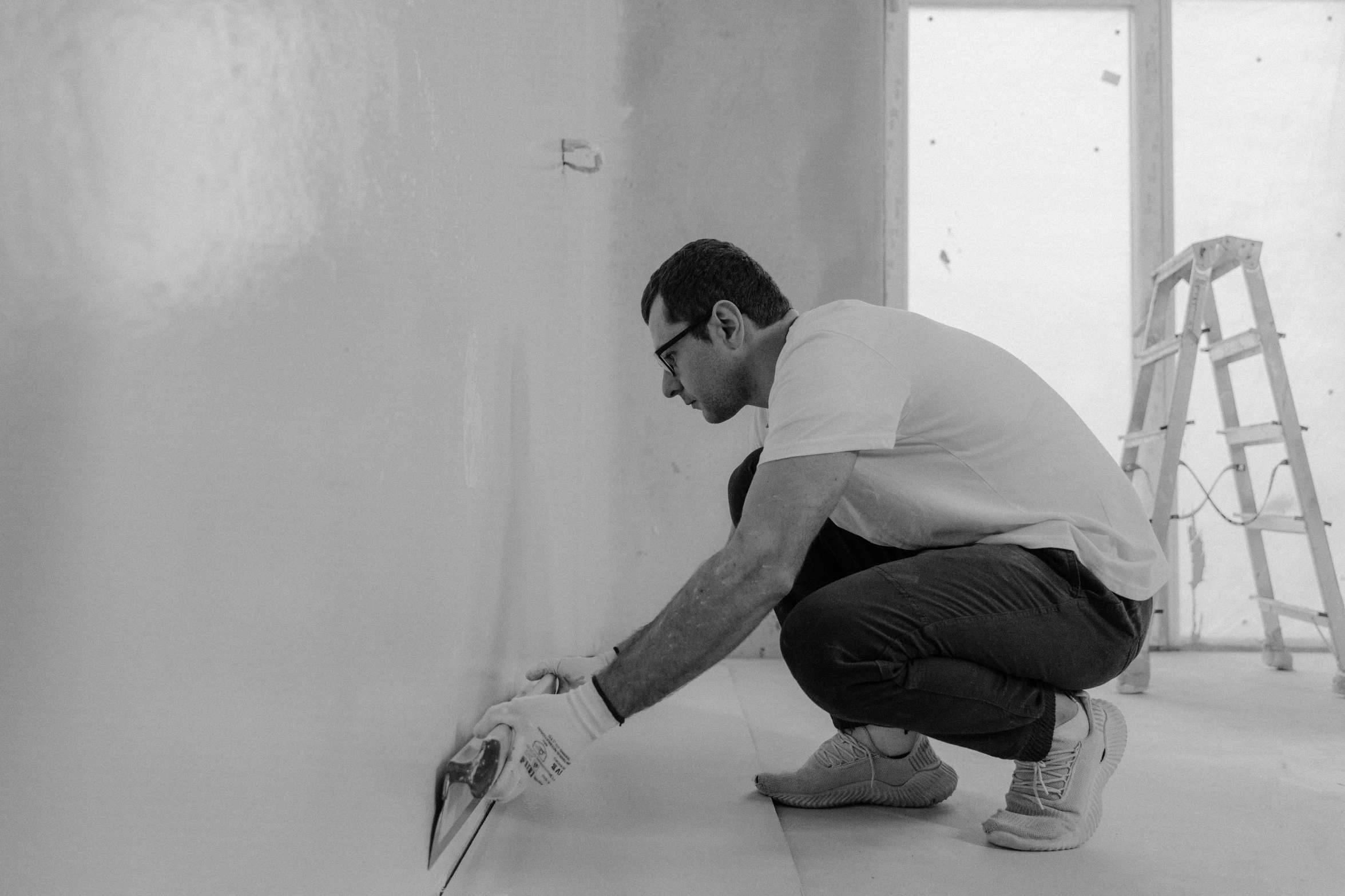 a man kneeling down with a pair of scissors in his hand, a black and white photo, walls are made of dry wall, 15081959 21121991 01012000 4k, maintenance photo, physical painting