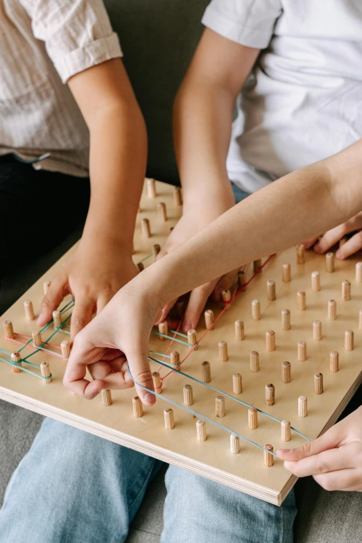 a group of people sitting on a couch playing a board game, by Jessie Algie, trending on pexels, interactive art, string art, holding a wood piece, little kid, square lines