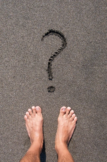 a person standing on a beach with a question mark in the sand, by Daniel Gelon, pexels contest winner, renaissance, exposed toes, on a gray background, slate, customers