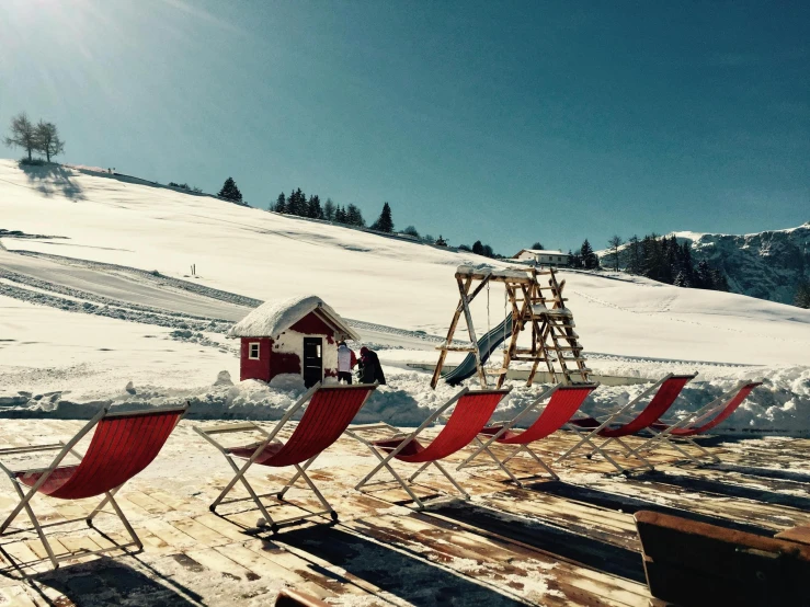 a row of lawn chairs sitting on top of a snow covered slope, by Matthias Stom, pexels contest winner, al fresco, chalet, crimson themed, in a sun lounger